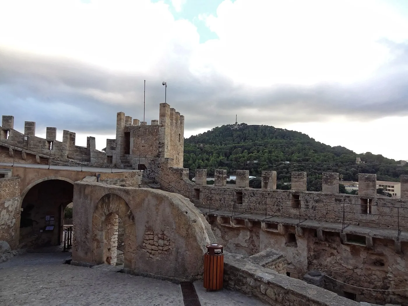 Zinnenmauer, Torbogen und Turm des Castell de Capdepera, dahinter ein bewaldeter Hügel