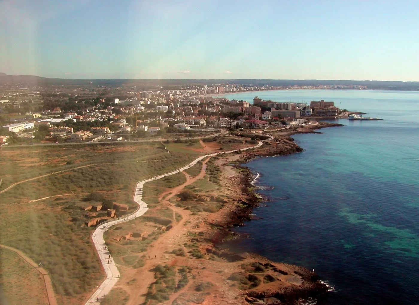 Felsige Küste von Es Carnatge mit Küstenweg, dahinter Häuser an der Bucht von Palma