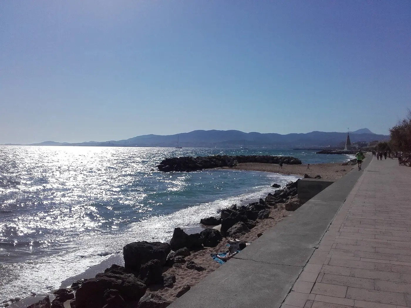Uferpromenade in Portixol mit Felsen, Meer und den Bergen der Bucht von Palma im Hintergrund
