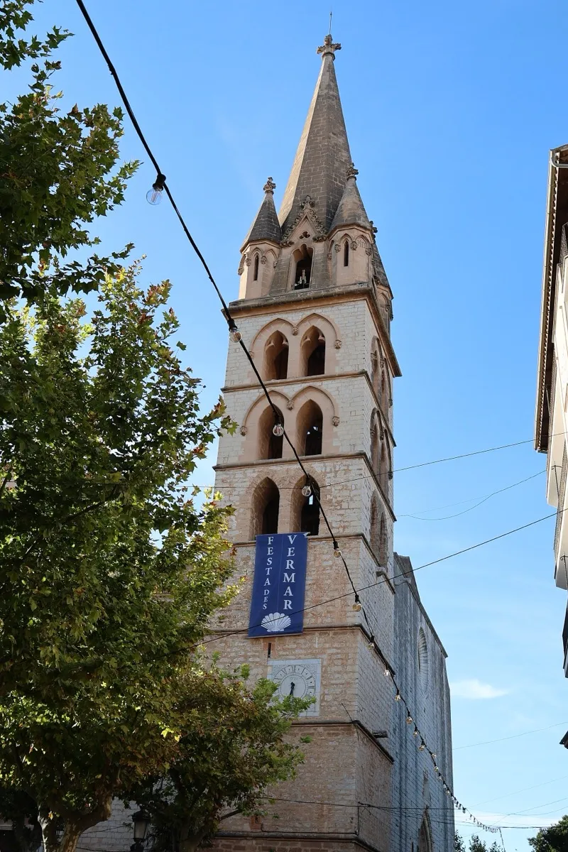 Gotischer Kirchturm von Binissalem mit Fahne der Weinlese vor blauem Himmel
